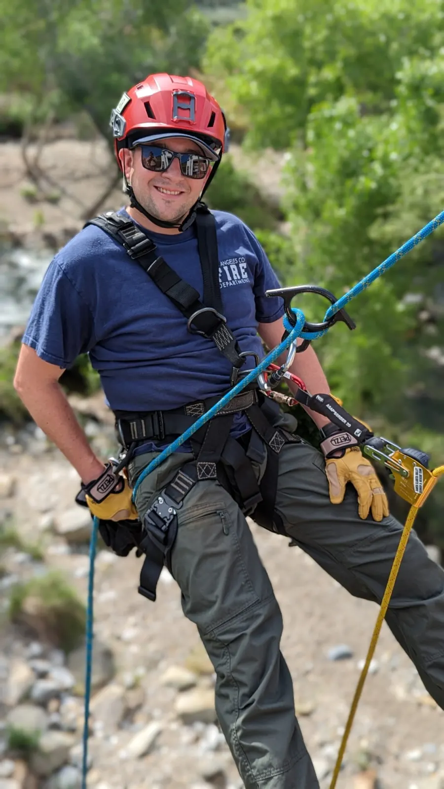 A smiling team member in a red helmet rappelling down a canyon wall